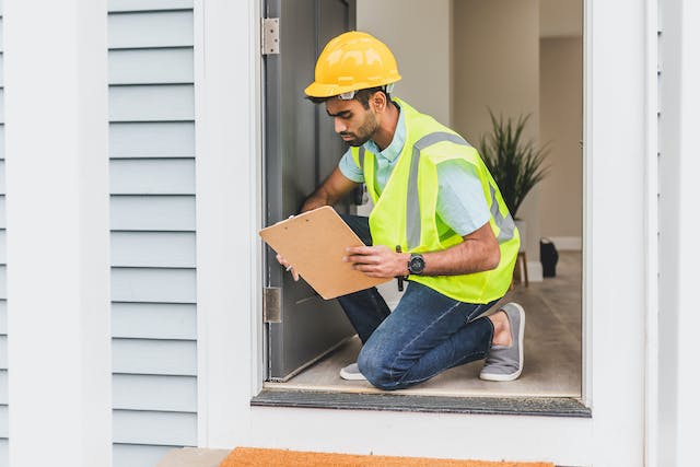 Person in a Neon Safety Vest and Checklist Inspeecting a Doorframe